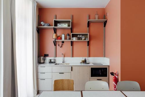 a kitchen with orange walls and a sink and chairs at Hôtel Préfecture - Entrée autonome, réception en ligne - Encore Mieux in Limoges