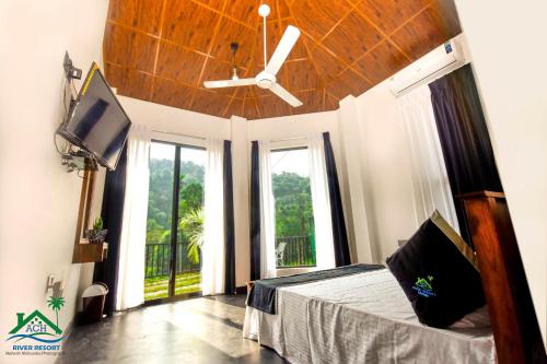 a bedroom with a bed with a ceiling fan and windows at ACH RIVER RESORT in Rattota