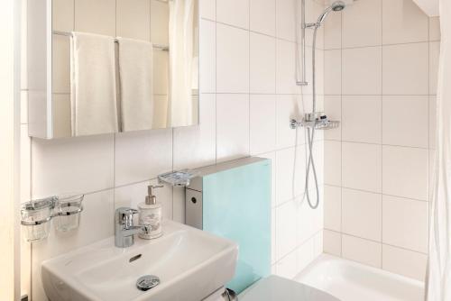 La salle de bains blanche est pourvue d'un lavabo et d'une douche. dans l'établissement La Petite Grange, à Villars-sur-Ollon