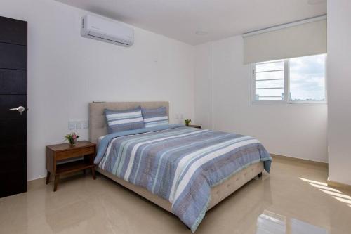 a white bedroom with a bed and a night stand at Amara, depa con vista al mar in Cancún