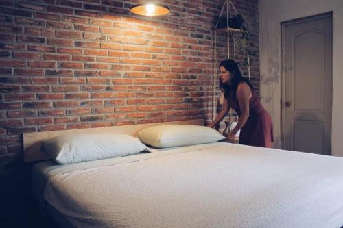 a woman standing next to a brick wall with a bed at Hoja Santa Posada in Cholula