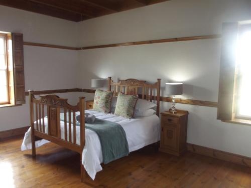 sypialnia z drewnianym łóżkiem z białą pościelą i poduszkami w obiekcie Bo-Plaas Farmhouse w mieście Bredasdorp