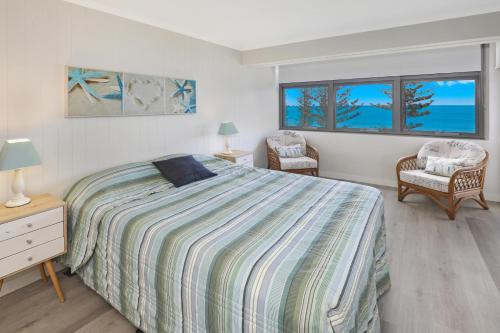 a bedroom with a bed and two chairs and two windows at Spinnaker Beach Front in Mooloolaba