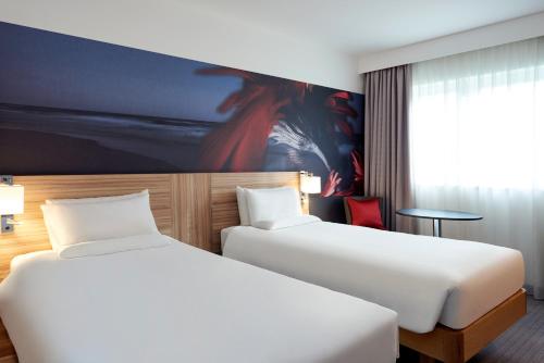two beds in a hotel room next to a window at Novotel London Stansted Airport in Stansted Mountfitchet