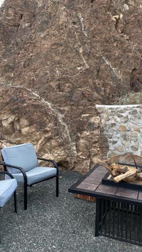 two chairs and a table in front of a stone wall at Alhara Lodge استراحة الحارة in Hatta
