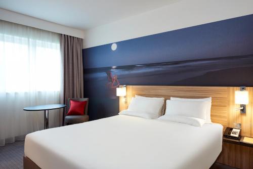 a hotel room with a large bed and a red chair at Novotel London Stansted Airport in Stansted Mountfitchet