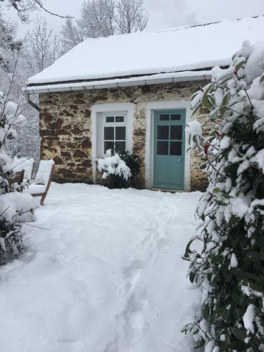 Cabaña de piedra con puerta verde en la nieve en Gites Libellule, en Aleu