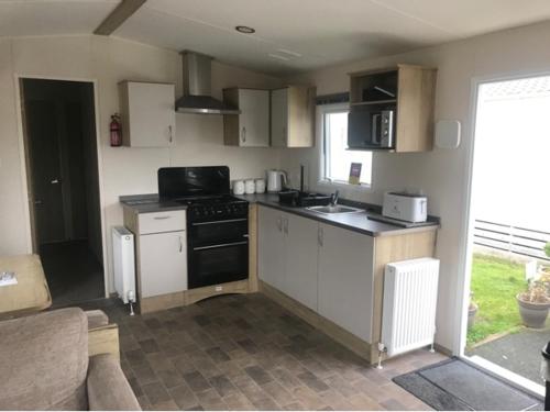 a kitchen with white cabinets and a black stove top oven at A family-friendly, eight birth, 2019 Abbey Trieste Caravan in Morecambe