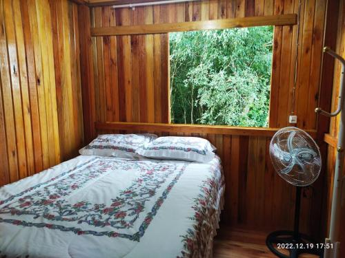 Cama en habitación de madera con ventana en Cabana, lagoas e natureza!, en Relvado