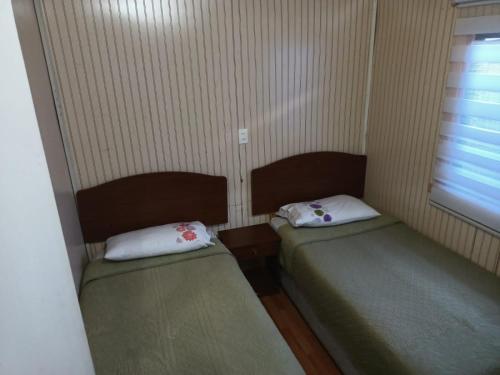 two beds in a small room with a window at Cabañas Érica in Choshuenco