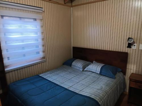 a bedroom with a bed with a blue comforter and a window at Cabañas Érica in Choshuenco