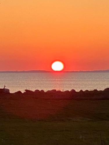 a sunset over the ocean with the sun setting at Hyggeligt Sommerhus med havudsigt in Humble