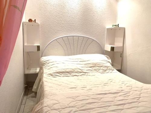 une chambre avec un lit blanc avec deux tables de nuit dans l'établissement Appartement F1 avec balcon et parking, à 5 min des Thermes et de l’Étang de Thau, animaux admis - FR-1-503-16, à Balaruc-les-Bains