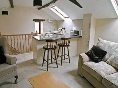 a living room with a couch and a kitchen at Orchard Cottage in Westward