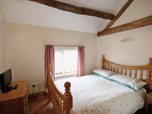 1 dormitorio con cama de madera y ventana en Tythe Barn, en Kingsley