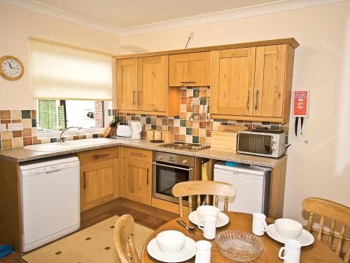 une cuisine avec des placards en bois et une table avec des chaises dans l'établissement Hollybush Cottage - E2800, à Cheddleton