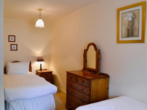 a bedroom with two beds and a dresser with a mirror at Freesia Cottage-mjd in Akeld