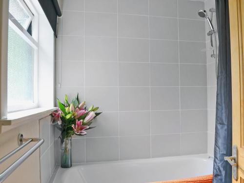 a white shower with a vase of flowers in a bathroom at Kinnettas Cottage in Strathpeffer