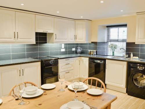 uma cozinha com uma mesa de madeira e cadeiras com copos em Longcroft Cottage - 28233 em Old Rayne