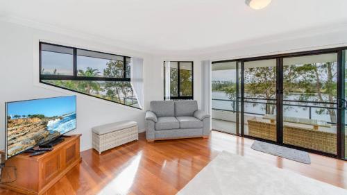 a living room with a tv and a chair and windows at Taroona in Yamba