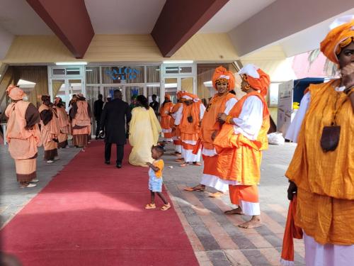 a group of people dressed in orange standing on a red carpet at Casa Djoko in Dakar
