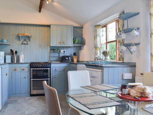 een keuken met blauwe kasten en een glazen tafel bij Mill Batch Cottage in Mark