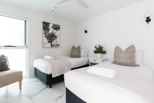 two beds in a room with white walls at One Marola is stylish privacy in paradise in Noosa Heads