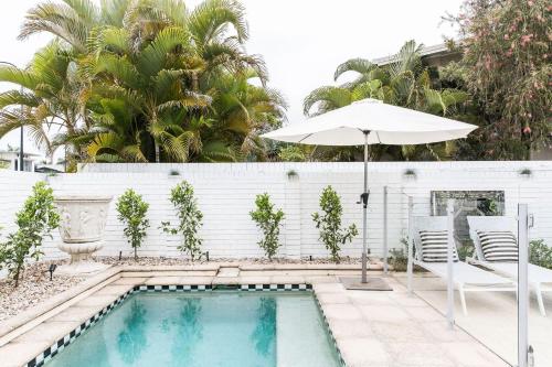 a swimming pool with an umbrella and two chairs and a white fence at One Marola is stylish privacy in paradise in Noosa Heads