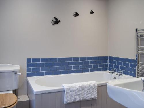 a bathroom with a white tub and blue tiles at Gable End Cottage in Goathland