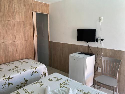um quarto com duas camas e uma televisão e uma cadeira em Pousada Savoya em Ilhéus