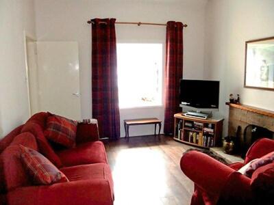 a living room with a red couch and a television at Brightwater Cottage in Arnisdale