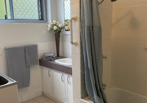 a bathroom with a sink and a shower with a vase of flowers at Aqua on Bribie 100 metres to Beach and Shops in Bongaree