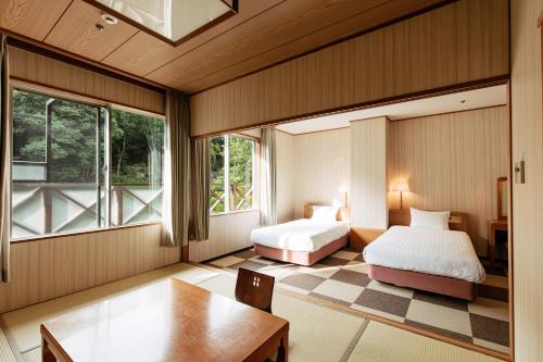 a bedroom with two beds and a table and windows at KAMENOI HOTEL Arima in Kobe