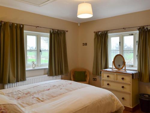 a bedroom with a bed and a mirror and windows at Watermill Cottage in Hargrave