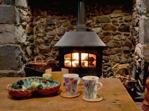a table with two cups and a bowl of food and a fireplace at Is Helen Cottage in Caernarfon