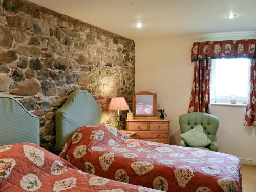 a bedroom with two beds and a stone wall at The Old Stables in Uldale