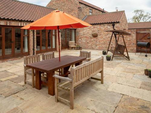 a wooden table with an umbrella on a patio at Wheelhouse Cottage . A brick-built barn conversion in Thirsk