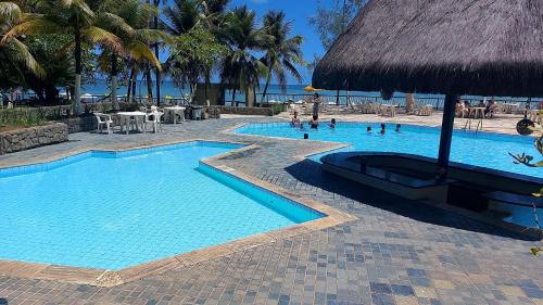 a swimming pool with a straw umbrella and a resort at QUARTOS em APARTAMENTO COMPARTILHADO BEIRA MAR in Recife