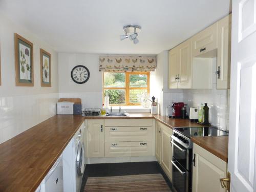 a kitchen with white cabinets and a clock on the wall at Grain Store 1 - 29635 in Portloe