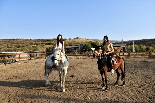 two women riding horses in a dirt field at Mankus Eco Park in Dzoraghpʼyur