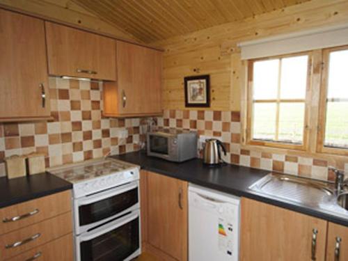 a kitchen with wooden cabinets and a stove and microwave at Field Lodge - E4380 in Overseal