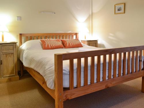 a bedroom with a wooden bed with white sheets and orange pillows at Rhydlanfair Cottage in Capel Garmon