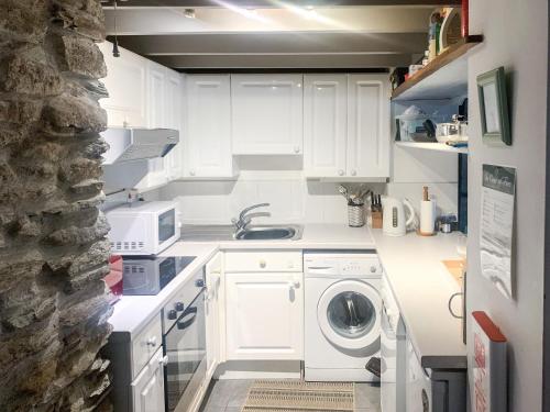 a white kitchen with a washing machine in it at Dawn Cottage in Portmellon