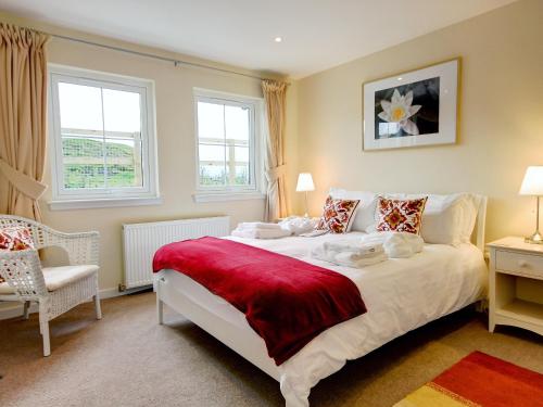 um quarto com uma grande cama branca e uma cadeira em Buzzard Cottages - 27940 em Cambusbarron