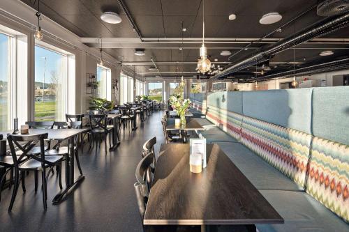 a restaurant with wooden tables and chairs and windows at Aiden by Best Western Trondheim Airport in Stjoerdal