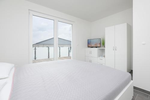 ein weißes Schlafzimmer mit einem großen Bett und einem Fenster in der Unterkunft Brenkenhagener Weg 4 Wohnung 7 in Grömitz