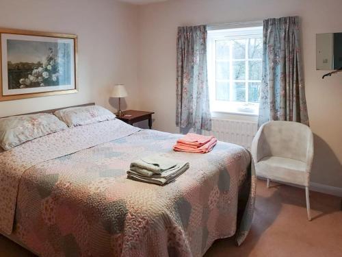 a bedroom with a bed with a chair and a window at Beck Cottage in Colby