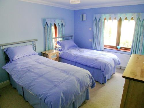 two beds in a bedroom with blue walls and windows at Bank End in Glenridding