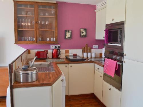cocina con armarios blancos y pared púrpura en Dynamo Cottage, en St Margarets at Cliff