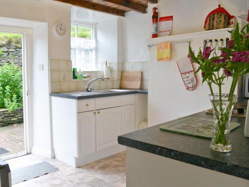 una cucina con armadi bianchi e un vaso di fiori di Ingle Neuk Cottage a Mosedale